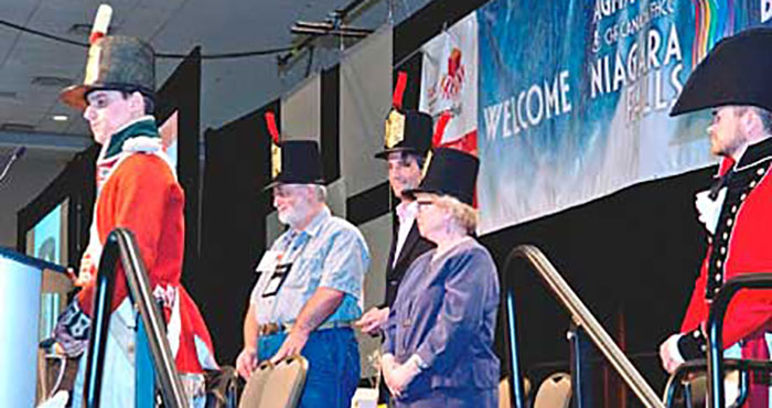 Meeting chairs, Bruce Woodrow, Geoffrey Dabbs and Noreen Dunphy receive their headgear during the traditional hat ceremony themed on the War of 1812.