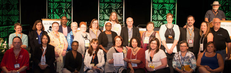 A group of co-op member sit and stand together in front of the podium at a CHF Canada AGM