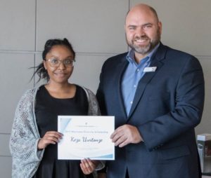 A young Black woman and a white man in a suit pose with a certificate