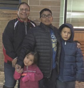 A family of four stand together in winter clothing outside a co-op.