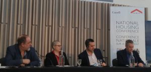 Four people speak on a panel, beside a sign that reads "National Housing Conference"