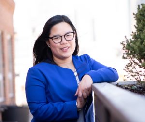 A young woman in a blue sweater poses on a rooftop patio