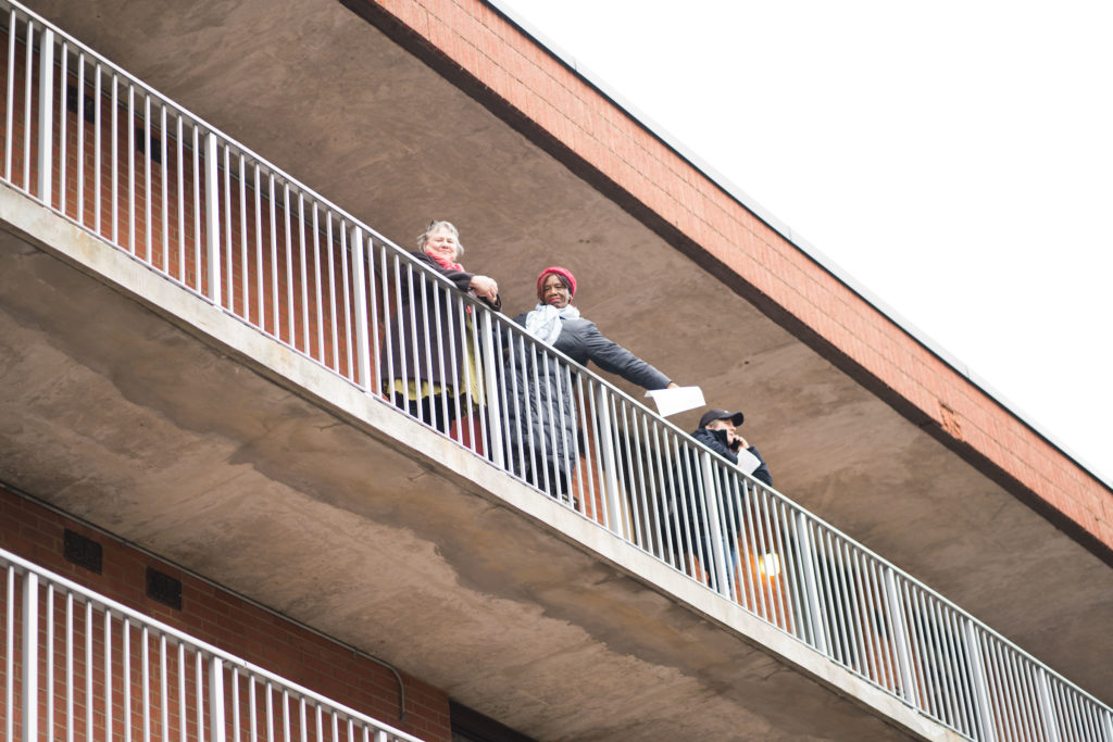 Three people pose on a balcony, shot from below