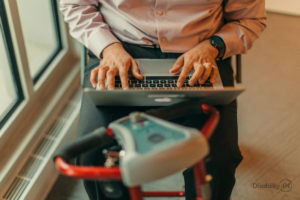 A person using a mobility scooter types on a laptop