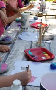 Hands of adults and children are shown as they work on paintings at a picnic table