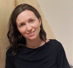 Dallas, a white woman with shoulder-length brown hair, wearing a dark grey blouse, smiles into the camera.