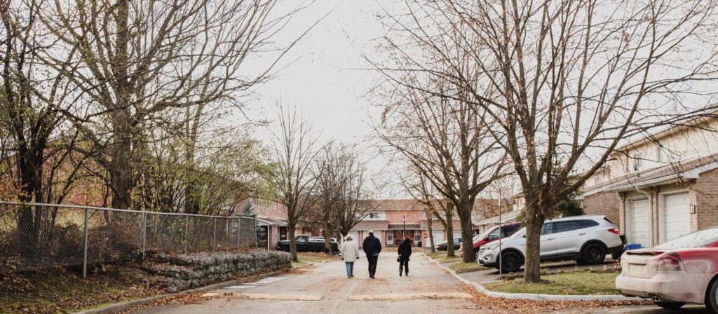 Three people in the distance walk down a street with co-op homes and mature trees on either side