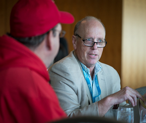 A white man with glasses speaks with a co-op member in a read sweater and hat