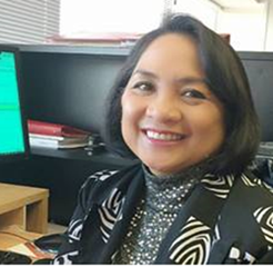 A woman with dark bobbed hair smiles at her desk