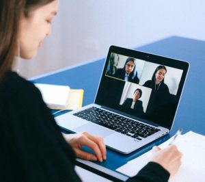 A person with long hair is on a Zoom meeting, with three other people shown on the call