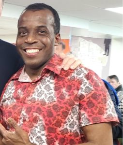 Dale, a Black man with a friendly smile, short hair, and a red and white button-up shirt