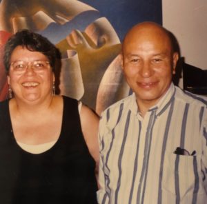 An older Indigenous couple smile, standing in front of a painting