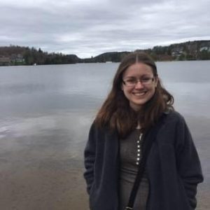 Christine, a young white woman with glasses and shoulder-length hair, stands by a lake