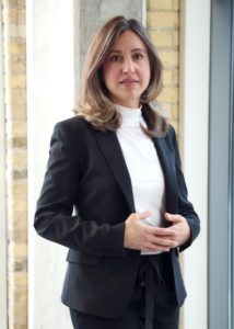 Jessica, a young white woman with shoulder-length hair, wears a blazer and stands by a window