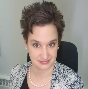 Headshot of Maria, who has short brown hair and wears a pearl necklace and patterened blazer