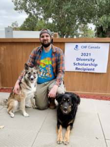 Dylan, with two dogs, kneels near a Diversity Scholarship banner