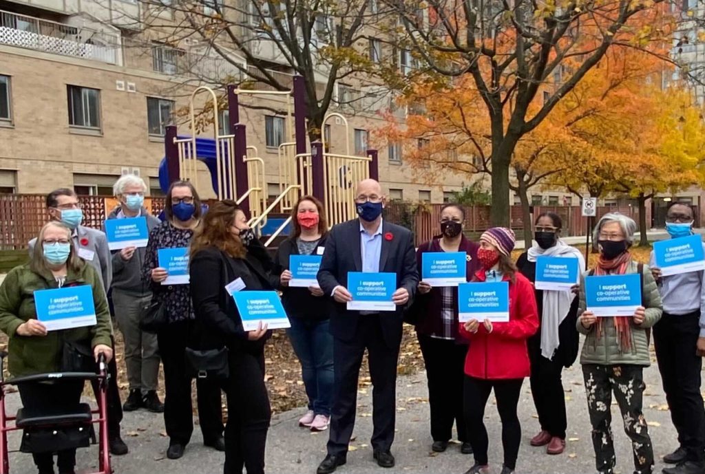 Ontario Minister Steve Clark stands outside Mimico Co-op in Etobicoke with members and co-op housing leaders. They hold signs that say "I support co-operative communities".