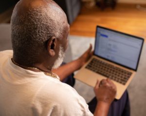 An older Black man uses a laptop, shown from behind