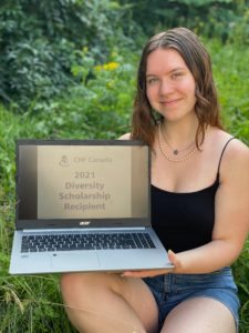 Emma, a young white woman with wavy hair, sits in a garden holding a laptop whose screen displays "2021 diversity scholarship recipient"