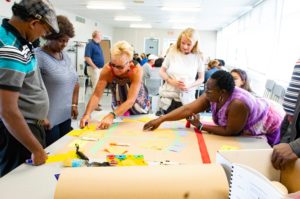 People gather around a large roll of paper collaboratively placing smaller colourful notes on it