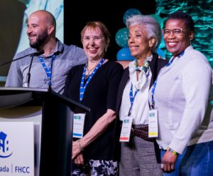 A man and 3 women stand on stage smile as they're applauded for receiving an award.