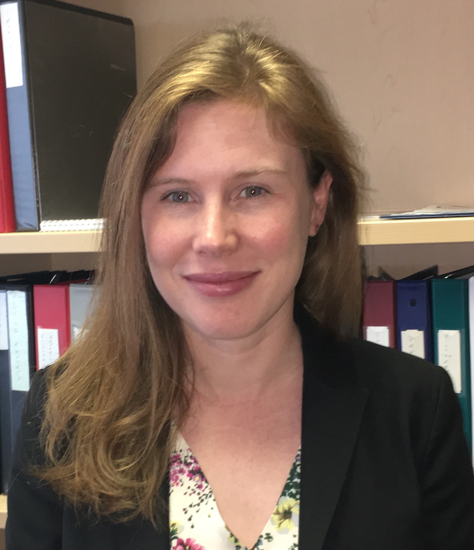 A woman stands smiling in front of a bookcase.