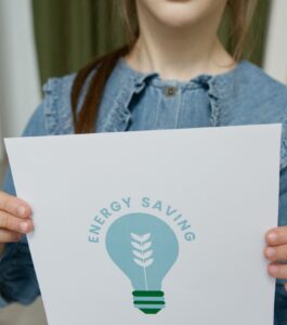 A girl holds a sign with a green lightbulb that says "energy saving"