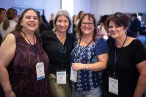 Four women wearing name badges stand together and smile at a professional Co-operative Housing event hosted by CHF Canada.
