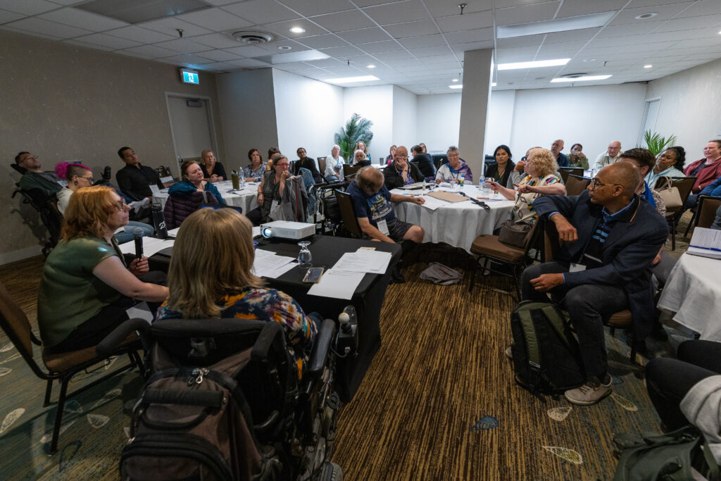 A group of people seated around tables in a conference room, engaged in discussion during a Co-operative Housing meeting or workshop.