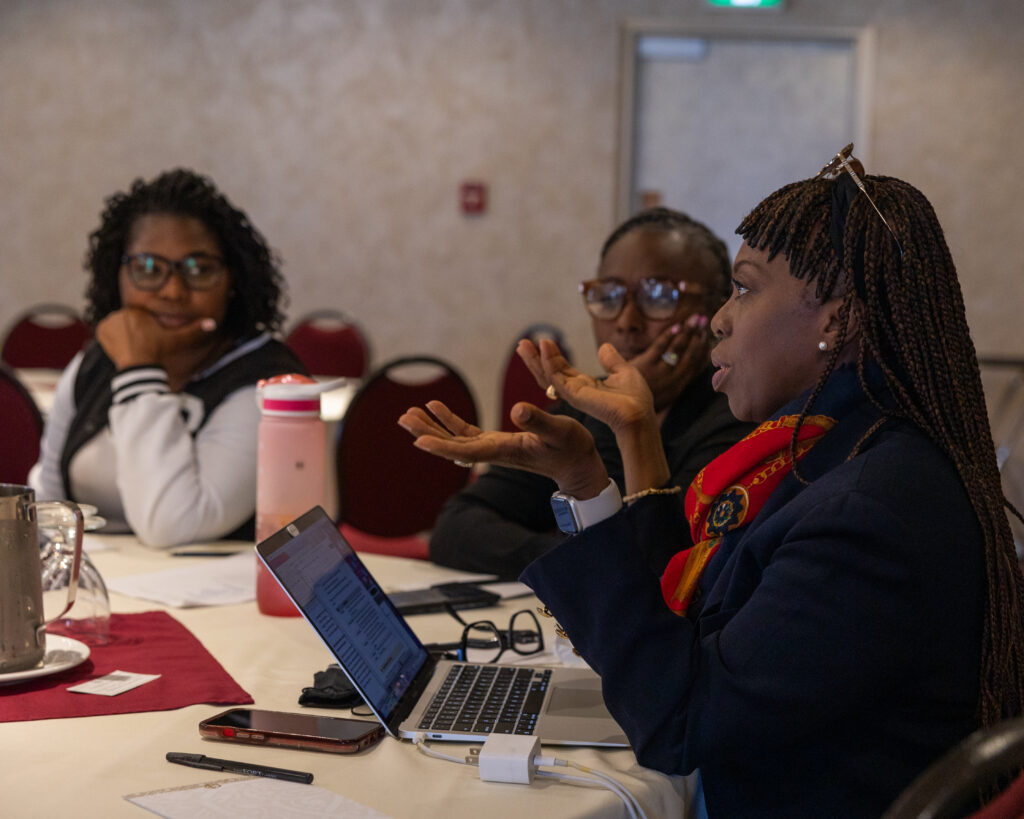 Three people sit at a table in discussion about co-operative housing, with a laptop, papers, and cups in front of them. One woman gestures while speaking, and the others listen attentively as they consider ideas from CHF Canada.