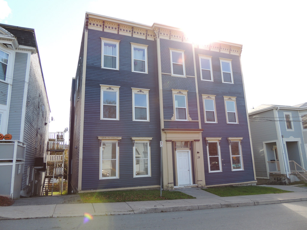 A three-story blue and beige Co-operative Housing apartment building with white trim and a central entrance, situated on a residential street in sunlight.