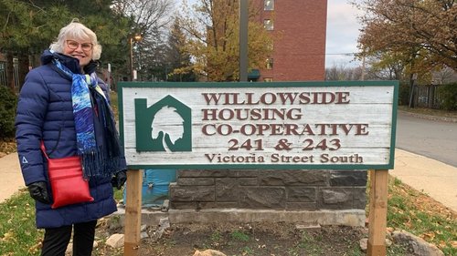 An older woman in a blue winter coat stands next to a sign for Willowside Co-operative Housing at 241 & 243 Victoria Street South, highlighting the spirit of CHF Canada communities.