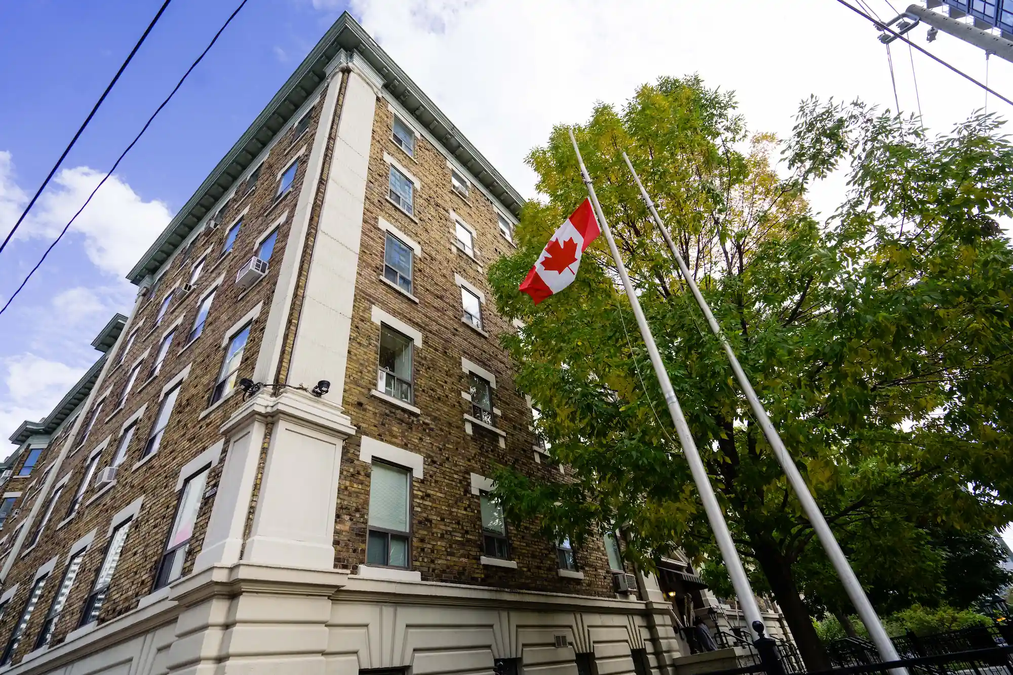 A Canadian flag flies at half-mast outside a multi-story brick co-operative housing apartment building, with green trees nearby.