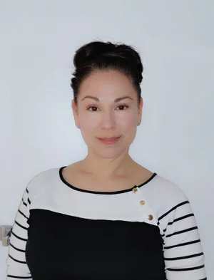Woman with dark hair pulled back, wearing a black and white striped top with gold buttons, stands against a plain white background—reflecting the confident spirit of co-operative housing and the vibrant community promoted by CHF Canada.